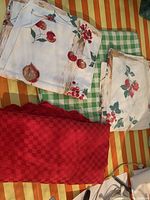 Photo showing all four vintage tablecloths folded: large red checkered, green and white checked, two smaller fruit motif cloths with cherries and berries on white background