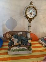 Full view of Whistling Willie figurine clock showing character reclining on bench holding newspaper and attached clock above.