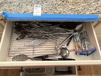 Drawer with stainless steel skewers, seafood crackers, perforated spoons, ladle, and some kitchen tools.