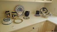 Wide view of all blue and white china dishes including plates, bowls, vases, pitcher, and canisters arranged on a white countertop.