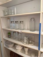 Multiple shelves showing glass canisters, pitchers, ceramic tureen, bowls, and trays