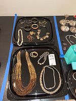 Two black trays with assortment of jewelry items showing necklaces and bracelets