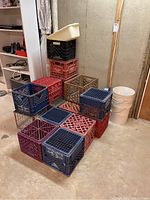Nine assorted milk crates stacked and arranged on basement concrete floor, plus four white buckets grouped on right side.