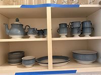 Photo showing teapot, creamers, and blue pedestal cups with saucers below on shelves