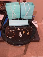 Photo showing all jewelry pieces arranged on a black tray with Tiffany & Co. gift bags and box in the background.