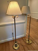 Both brass toned floor lamps side by side, showing bases, poles, and shades.