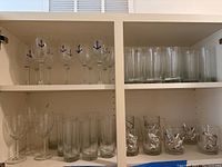 Full shelf view showing wine glasses with anchor design, plain tall glasses, and tumblers with raised nature designs.