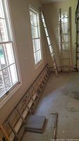 Photo showing the 12-foot aluminum extension ladder leaning against the wall, along with two 8-foot ladders lying horizontally on the floor.