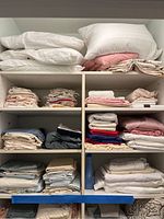 Shelves with stacked white pillows on top and various folded linens including sheets, kitchen towels, and table linens below.