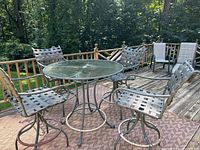 Full view of outdoor bistro table and four matching chairs on a deck with wooded background.