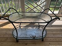 Full side view of the buffet cart showing two glass shelves, metal frame with handle bars and caster wheels.