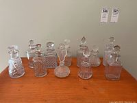 Full view of 10 vintage clear glass perfume and cologne bottles with glass stoppers on wooden surface
