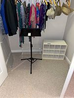 Photo of closet area showing all three items: black adjustable music stand in center, white wire rack shelf behind it, and white 12-cubby shoe shelf on right side.