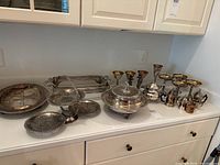 Wide view of various silver plated barware and serving pieces on counter showing champagne glasses, covered serving dish, tray and candlesticks.