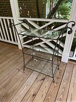 Full front left angle view showing three levels with glass shelves and black metal frame with decorative curl detail.