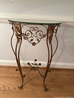 Full frontal side view of the demi lune table showing metal base with ornamental scrolls, leaves, and a flower detail near the bottom stretcher.