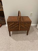 Front view of vintage wooden sewing box on legs with closed compartments and central handle