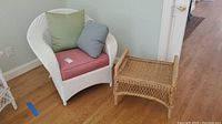 White wicker wingback chair with cushions and throw pillows, positioned near a wall and door.