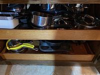 Photo showing shelves with stacked bakeware including muffin tin, colander, and pots and pans.