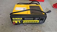 Top and front view of the yellow and black DeWalt battery charger showing brand, model, display, buttons and terminals.
