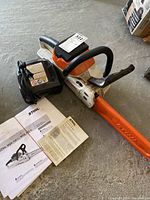 Overview of Stihl cordless chainsaw, battery charger and instruction manual on concrete floor