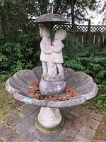 Front angle view of large concrete garden fountain showing children figurine and scalloped basin