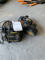 Photo showing two used DeWalt 18V batteries and the charger with cable on concrete floor.