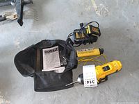 Photo of the cordless drill, charger, carrying bag, and user manual spread on concrete floor.
