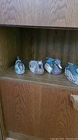 Photo showing four wooden duck decoys arranged side by side on a wooden shelf, displaying various duck types and colors.