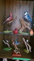 Shelf display showing multiple bird sculptures including a red cardinal, blue jay, and smaller birds on naturalistic wooden branches and bases