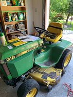 Front-left view of John Deere 318 tractor with yellow mower deck in garage.