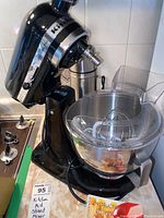 Full view of the black KitchenAid stand mixer with clear mixing bowl and metal Thermos in background.