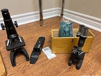 Wide view of all three microscopes with wood box and accessories on floor.