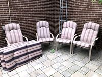 Photo showing four outdoor chairs with beige metal frames and striped brown and beige cushions. Also shows four extra striped cushions stacked next to the chairs.