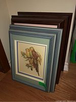 Three framed paper tole artworks stacked leaning against wall, showing various frame colors and artwork themes of birds and flowers