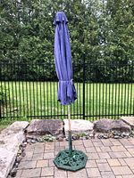 Full shot of closed blue patio umbrella with green cast iron base on patio stone flooring.