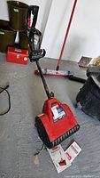 Full view of the red Toro Power Shovel with handle and control grips, showing the tool on a concrete floor alongside some other tools and containers.