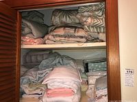 Shelf with multiple folded quilted coverlets and bedding items in various colors and patterns