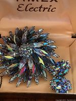 Brooch and single clip-on earring displayed inside a fabric-lined Timex Electric box