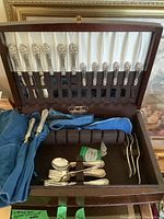 Open wood case showing upper and lower trays of sterling flatware and folded cloth