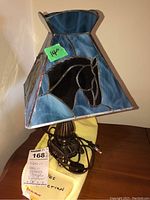Side view of the lamp showing the blue resin stained glass style shade with black horse design and bronze metal base.