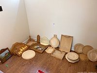 Wooden crafting items including plates, plaques, and trays arranged on a hardwood floor near a corner wall.