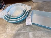 Set of four nested turquoise and white Pyrex bowls in Butterprint pattern with a rectangular snowflake baking dish nearby.