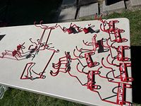 Overview of 21 red display hooks in varied sizes and shapes arranged on a white table, showing assortment for slat wall use.