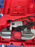 Open red plastic case showing one Milwaukee 6232-6N band saw with cord inside molded storage