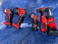 Six Milwaukee cordless work lights with various designs including spotlight, straight flashlight, right angle, and lantern style. All in red and black. Battery slots visible.