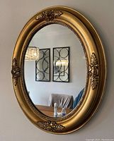 Full view of the antique oval carved wood mirror with gold frame and floral decoration hanging on a wall.