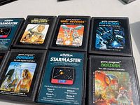 Photo showing eight Atari 2600 game cartridges including Warlords, Yars' Revenge, Berzerk, Defender, Starmaster, and Pac-Man with artwork and labels visible.