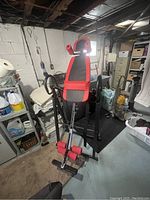 Overall view of the folding adjustable exercise equipment in a basement setting with black and red padded sections and steel frame.