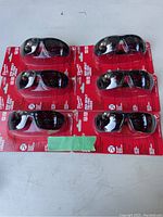 Six pairs of Milwaukee safety lenses in original red packaging arranged 3 rows by 2 columns on a gray surface.